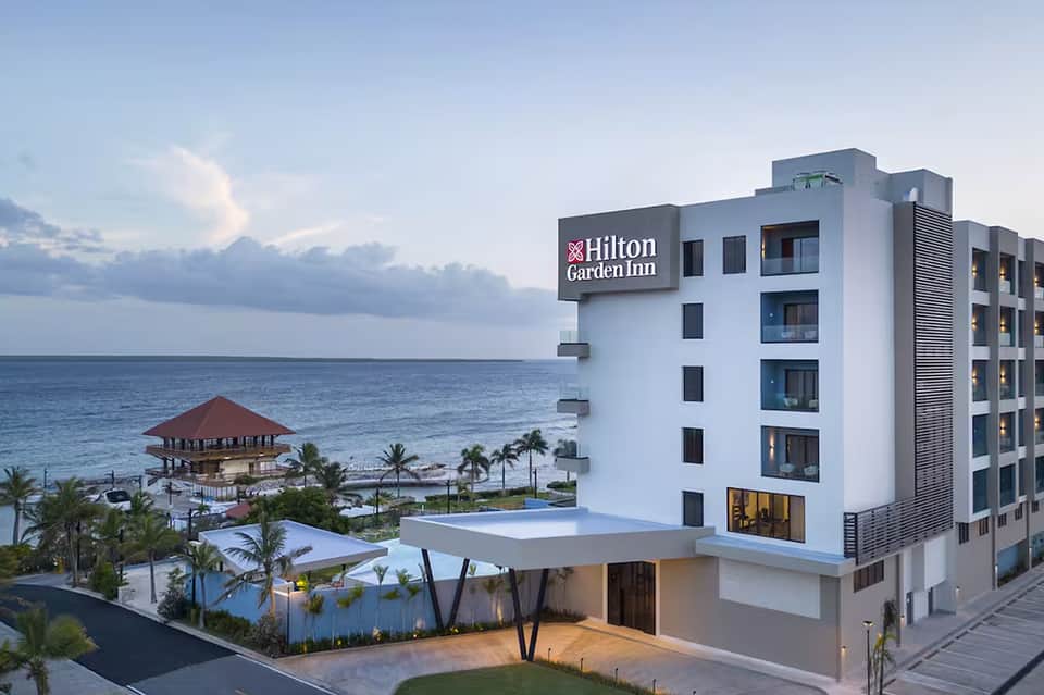 Hilton Garden Inn beachfront hotel at dusk with red-roofed pavilion and palm trees