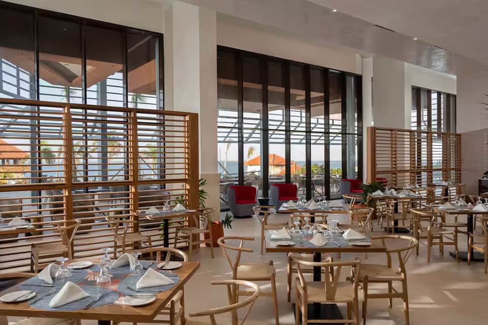 Fine dining restaurant with wooden chairs, round tables set with place settings, large windows with ocean views and wooden railings