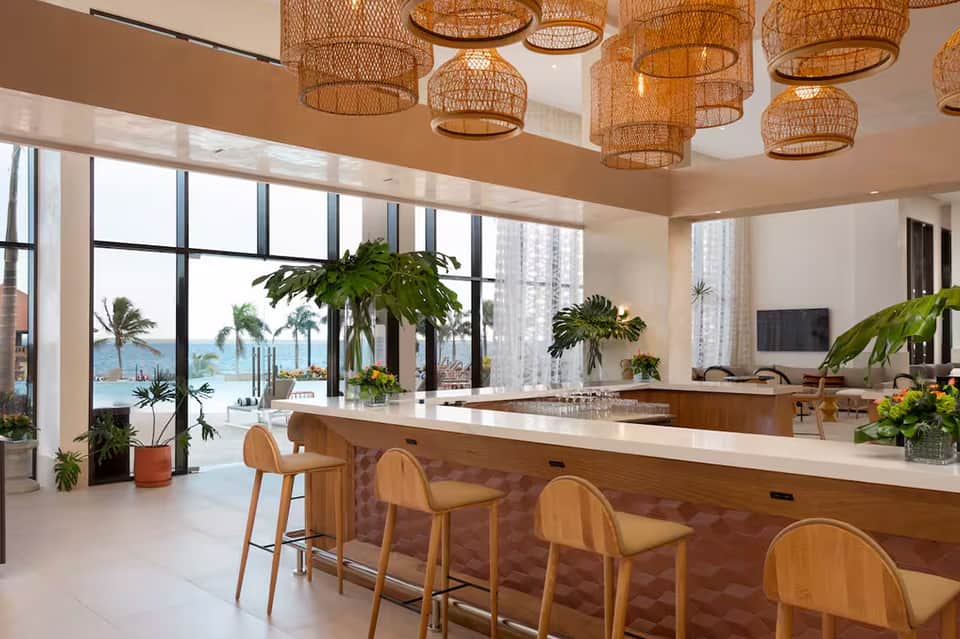 Luxury kitchen with woven pendant lights, white countertops, wooden bar seating, and ocean views through floor-to-ceiling windows