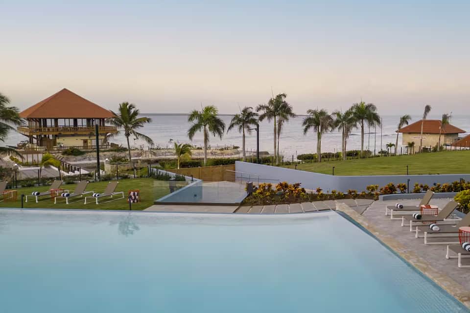 Beachfront resort with multiple blue pools, palm trees, ocean views, and tropical landscape at sunset