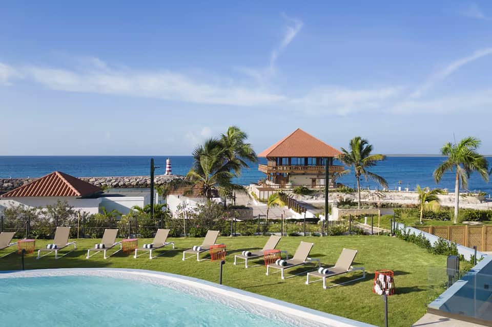 Beachfront resort with turquoise pool, loungers on manicured lawn, and ocean view