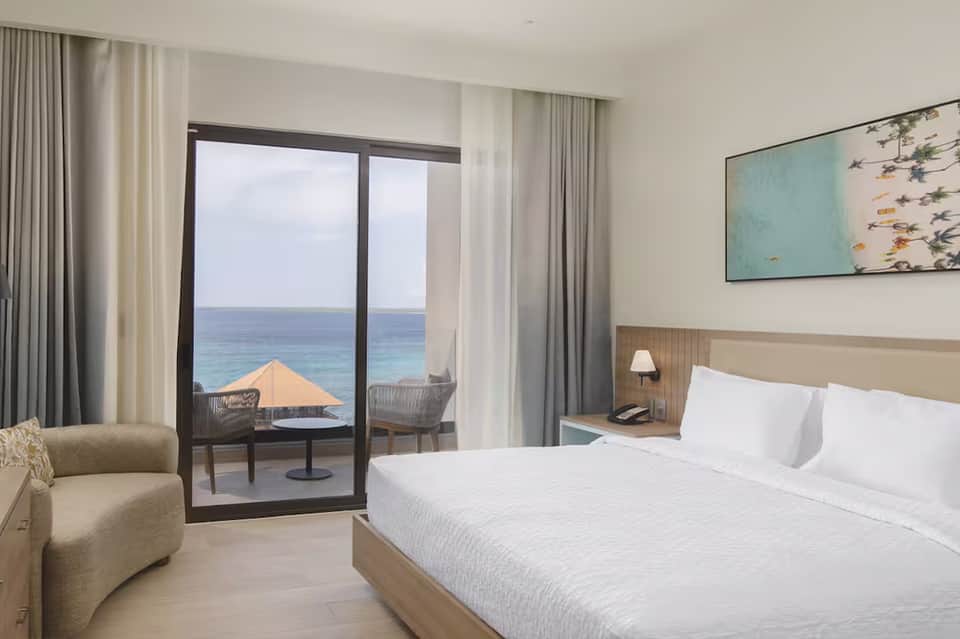 Beachfront hotel room with ocean view balcony, bed, and sitting area