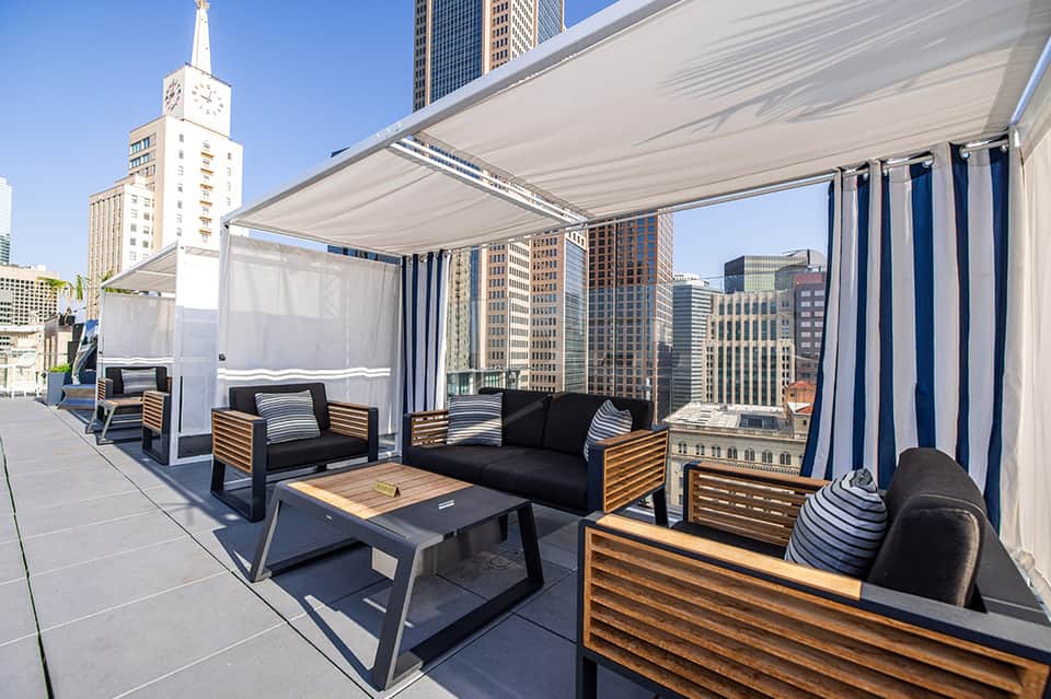 Urban rooftop lounge with modern furniture, retractable shade canopy, and city skyline views