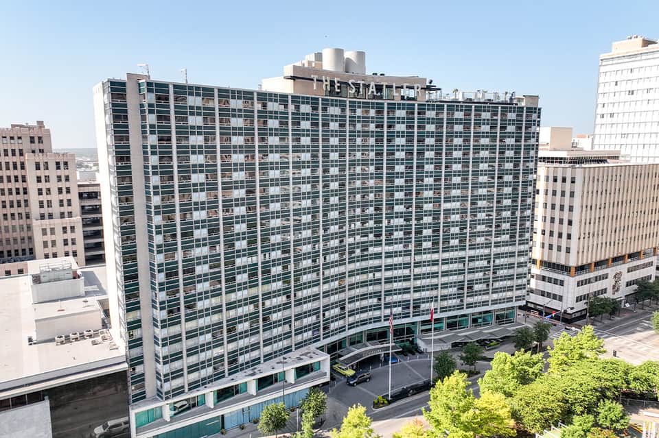 Tall residential high-rise building with blue-green glass facade surrounded by downtown urban architecture