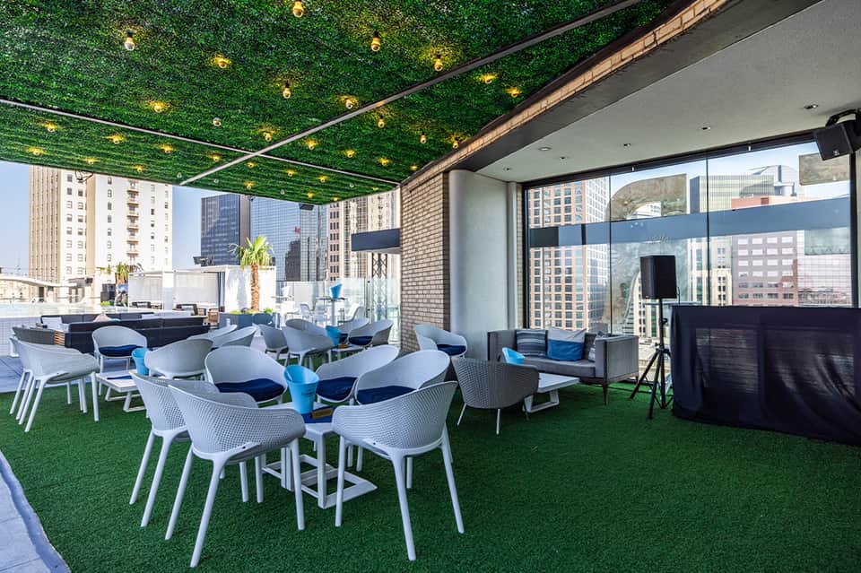 Rooftop terrace with artificial green turf, modern white chairs, dining tables, and city skyline views