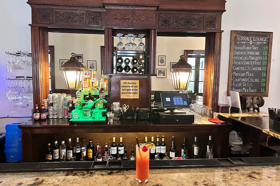 Upscale bar with ornate wooden mirror backdrop, illuminated green bottles, and colorful cocktail