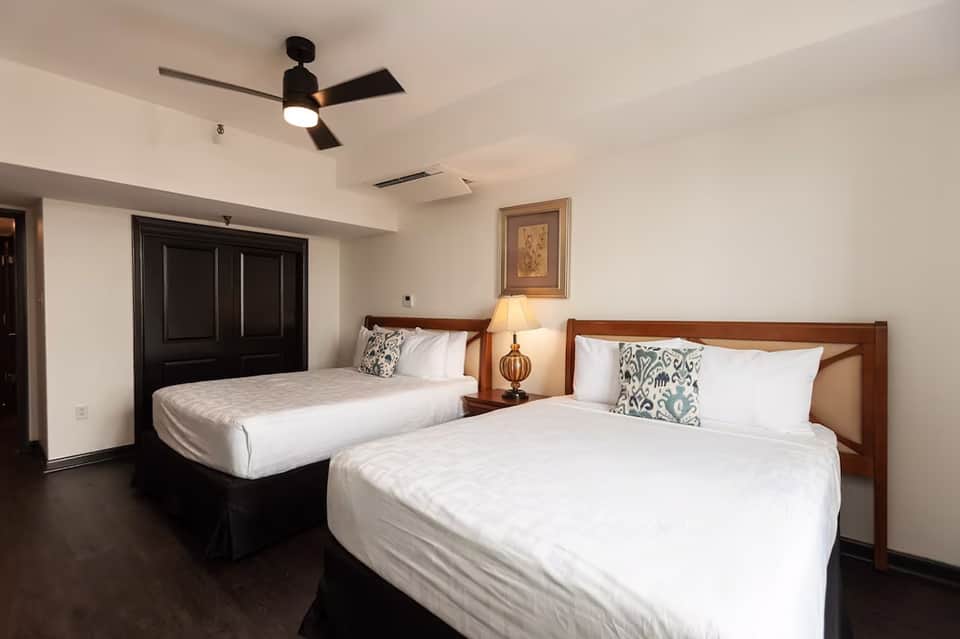Hotel bedroom with two queen beds, wooden frames, ceiling fan, and modern furnishings