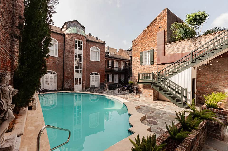 Outdoor pool surrounded by brick buildings, lounge chairs, and manicured landscaping in courtyard setting