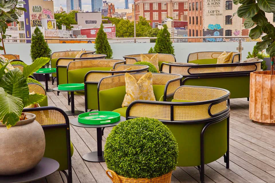 Rooftop lounge with green chairs, rattan details, and city skyline backdrop