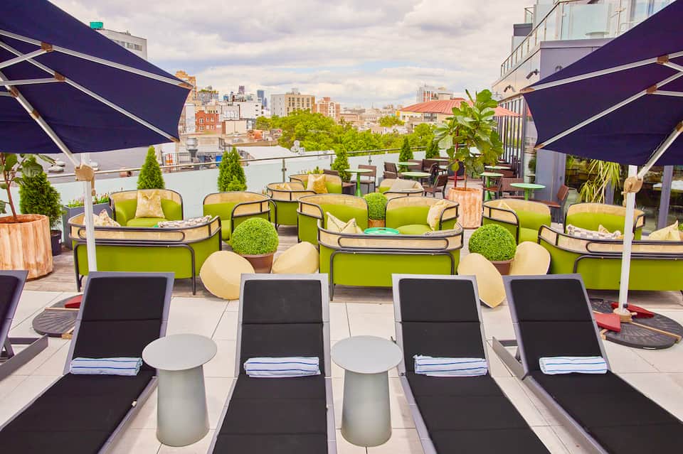 Urban rooftop lounge with lime green seating, navy umbrellas, and city skyline views