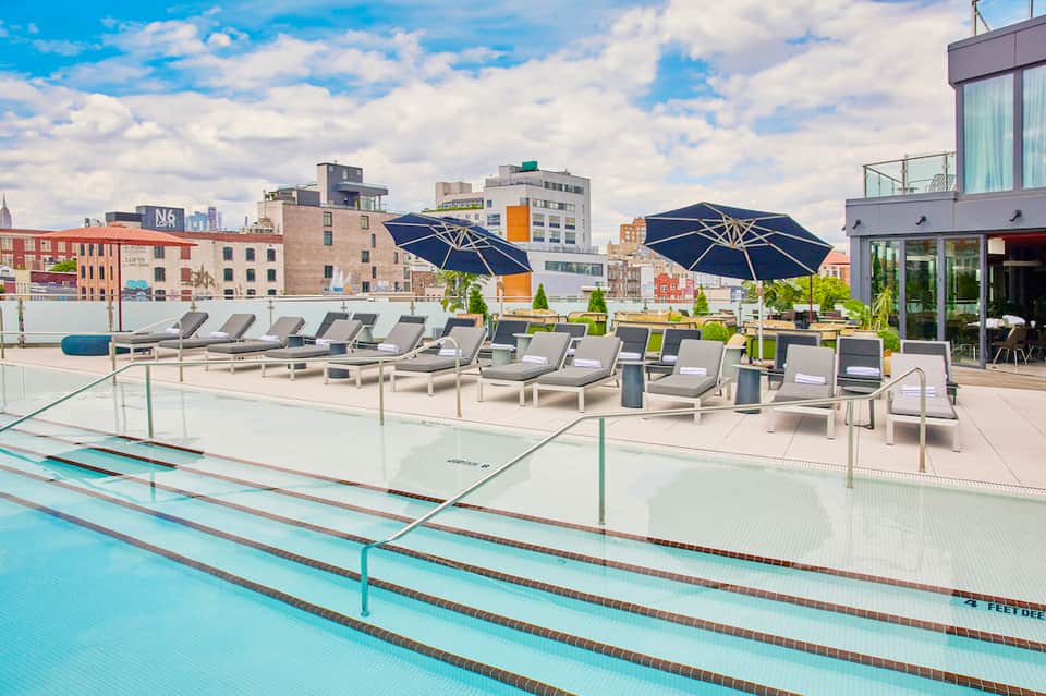 Rooftop pool deck with lap lanes, lounge chairs, navy umbrellas, and city skyline views