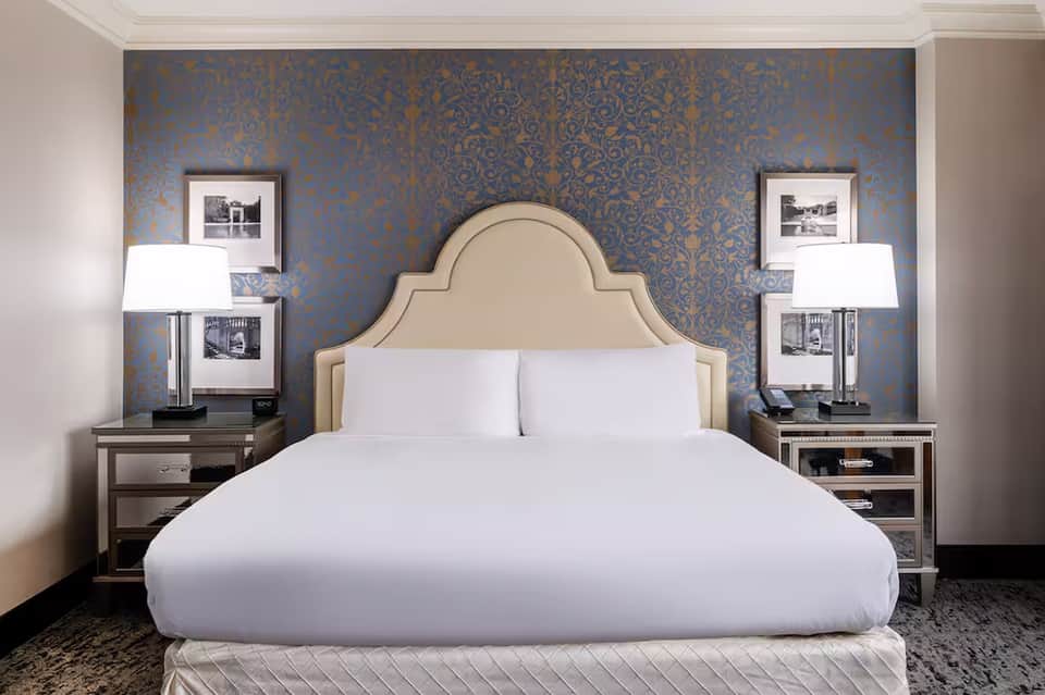 Elegant bedroom with cream upholstered headboard against blue damask wallpaper