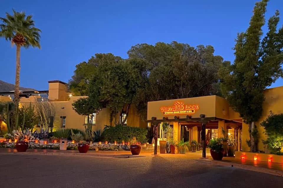 Yellow Spanish-style restaurant building illuminated at dusk with potted plants and palm trees