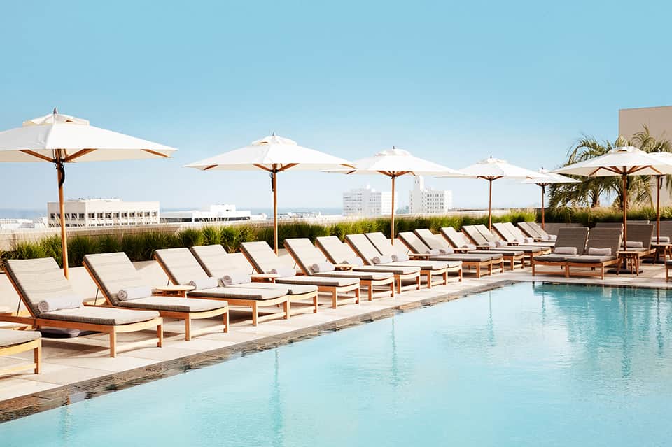 Luxurious rooftop pool with white umbrellas, wooden loungers, and city skyline views