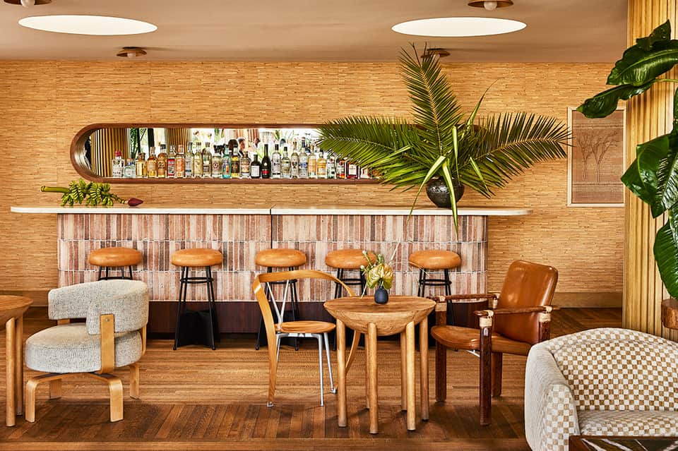 Modern hotel bar with wooden elements, leather stools, and tropical plants