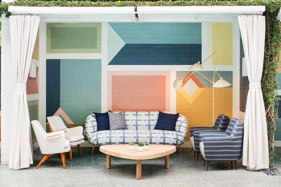 Modern lounge area with colorful geometric mural, patterned sofa, and mid-century armchairs around wooden coffee table