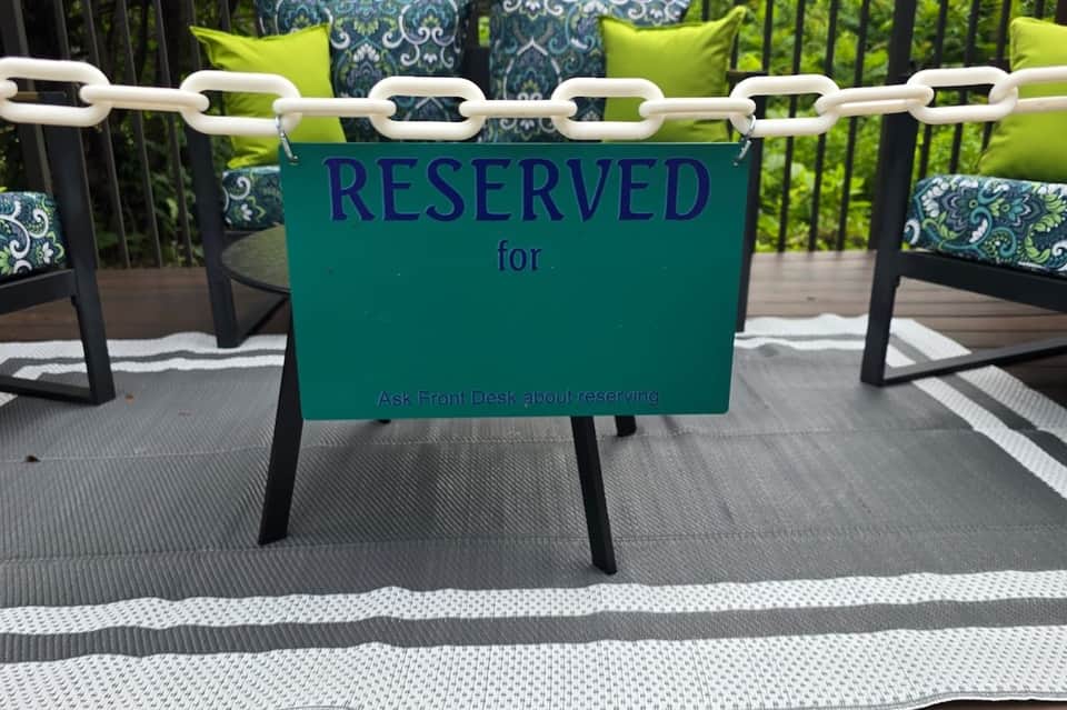 Green reserved seating sign on chain-link fence with cushioned lounge chairs on outdoor deck