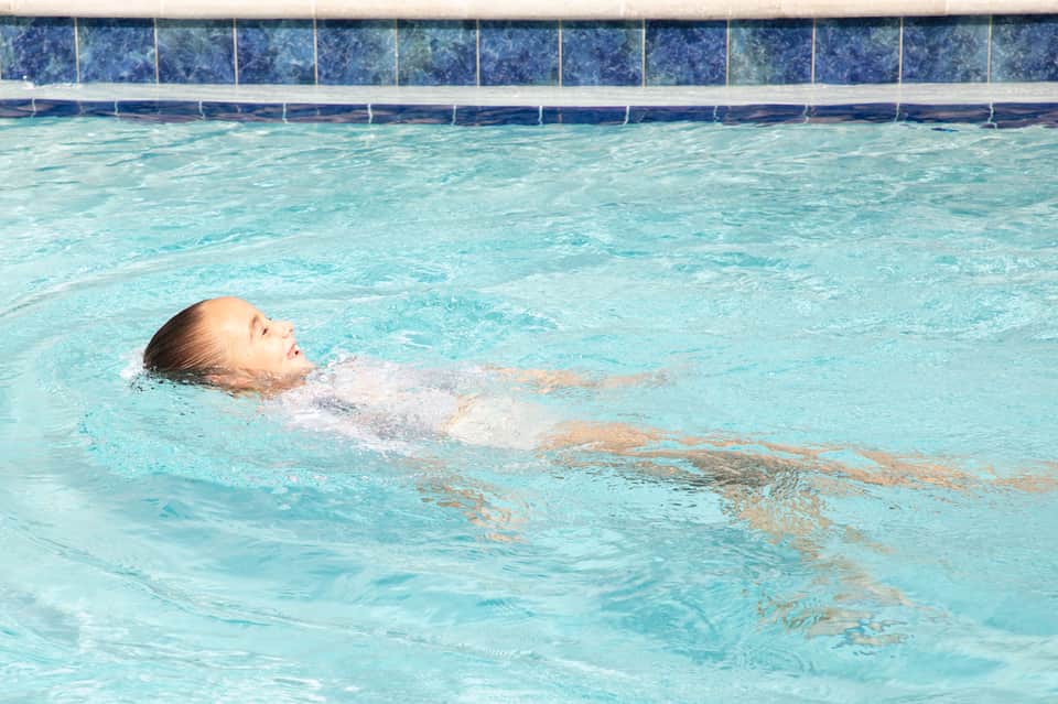 Person doing backstroke in bright turquoise pool with blue tile border