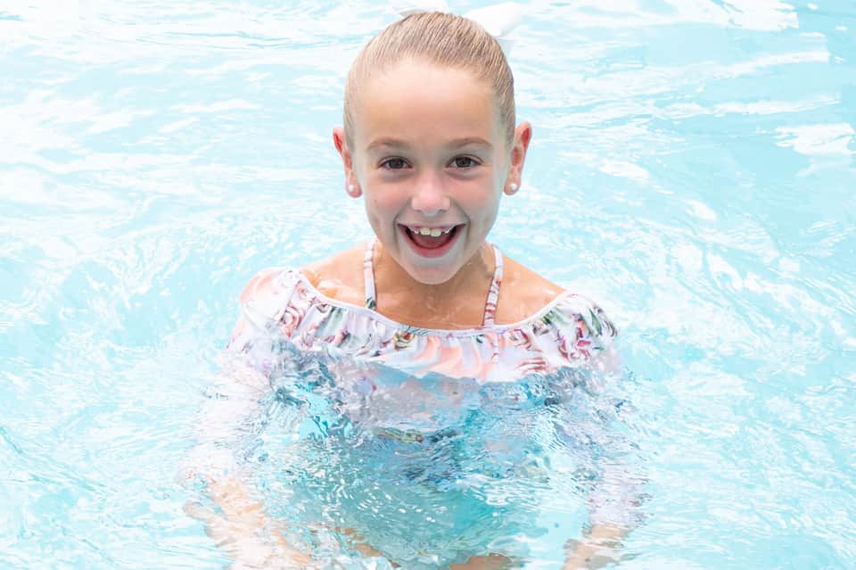 Young girl smiling in a swimming pool wearing a colorful swim shirt