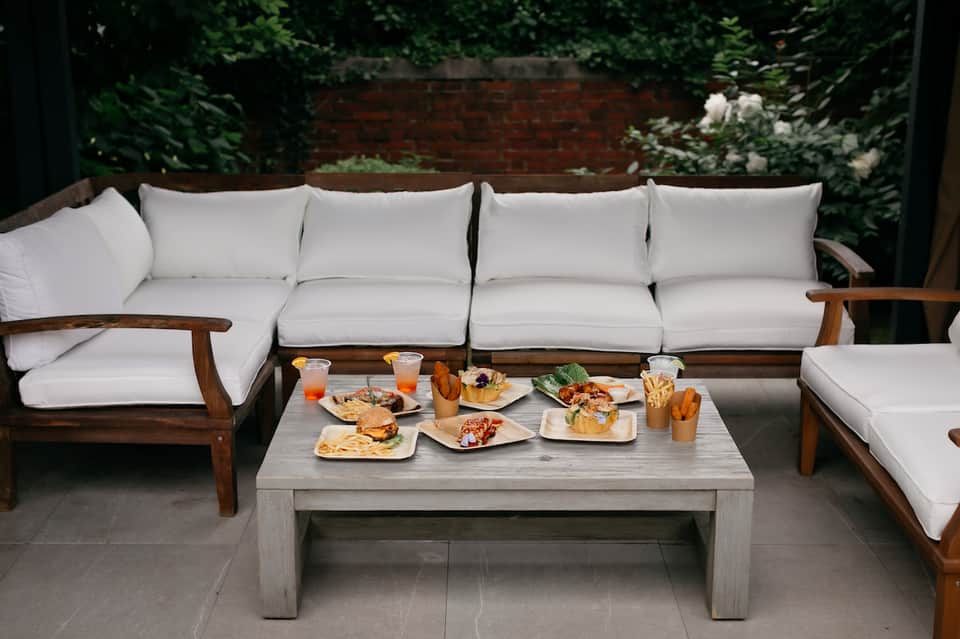 Wooden sectional sofa with white cushions and concrete table displaying appetizers and drinks