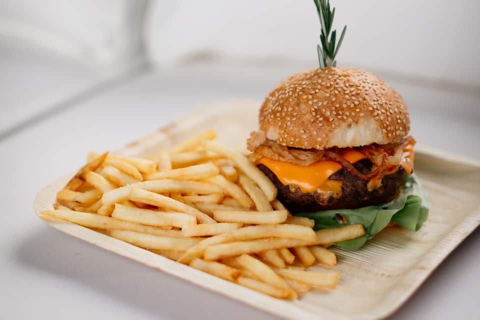 Gourmet burger with sesame seed bun, bacon, and cheese with french fries