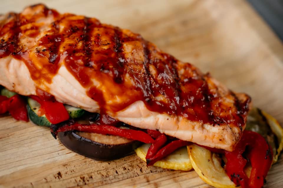 Glazed salmon fillet with roasted vegetables on wooden serving board