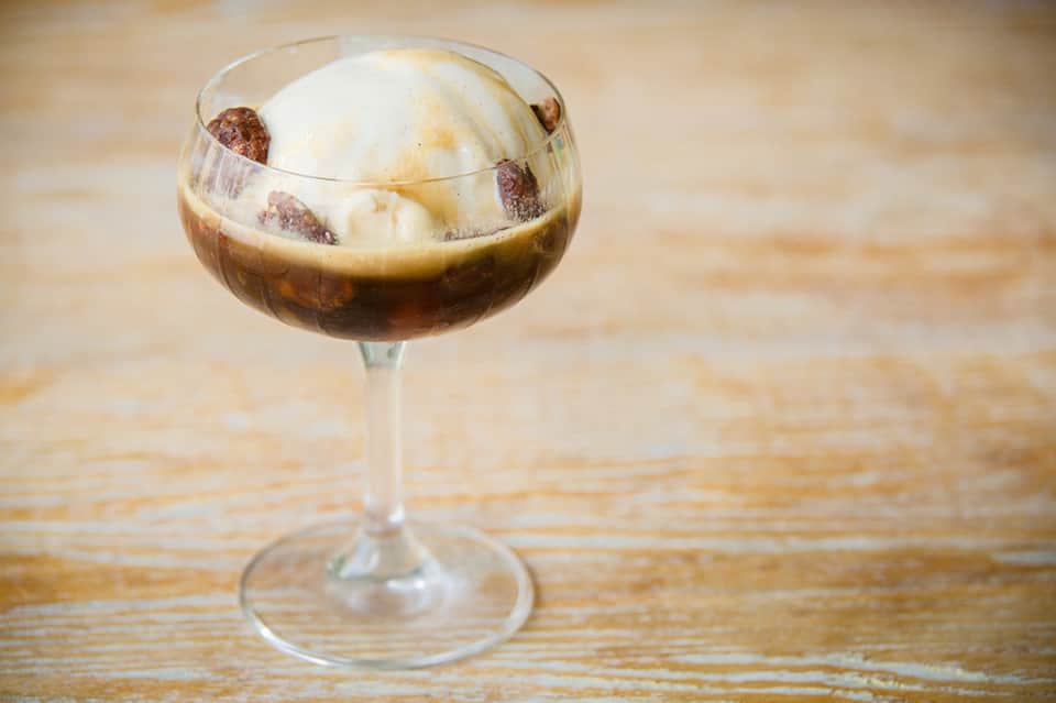 Espresso martini cocktail with whipped cream and coffee beans in coupe glass on wooden surface