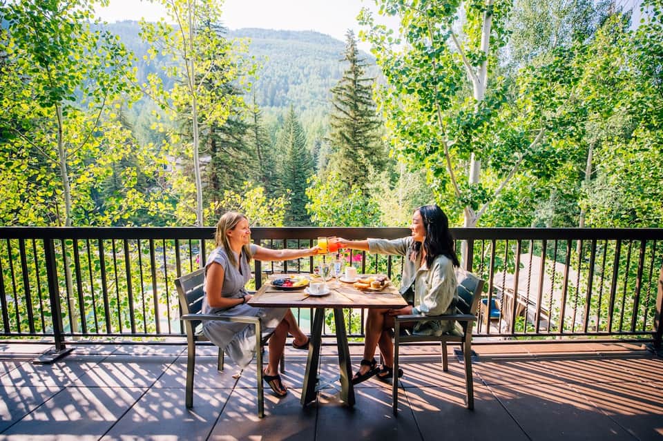 Two women dining on a mountain deck overlooking forested valley and distant peaks