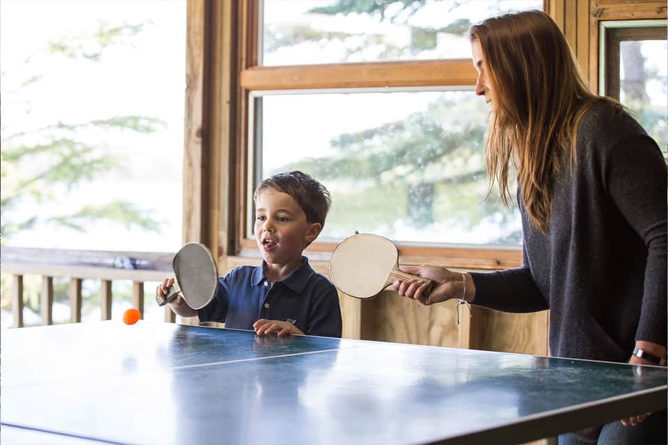 Woman and child playing table tennis indoors with mountain views through large windows
