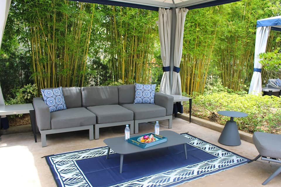 Outdoor patio with gray modular sofa under pergola surrounded by tall bamboo trees