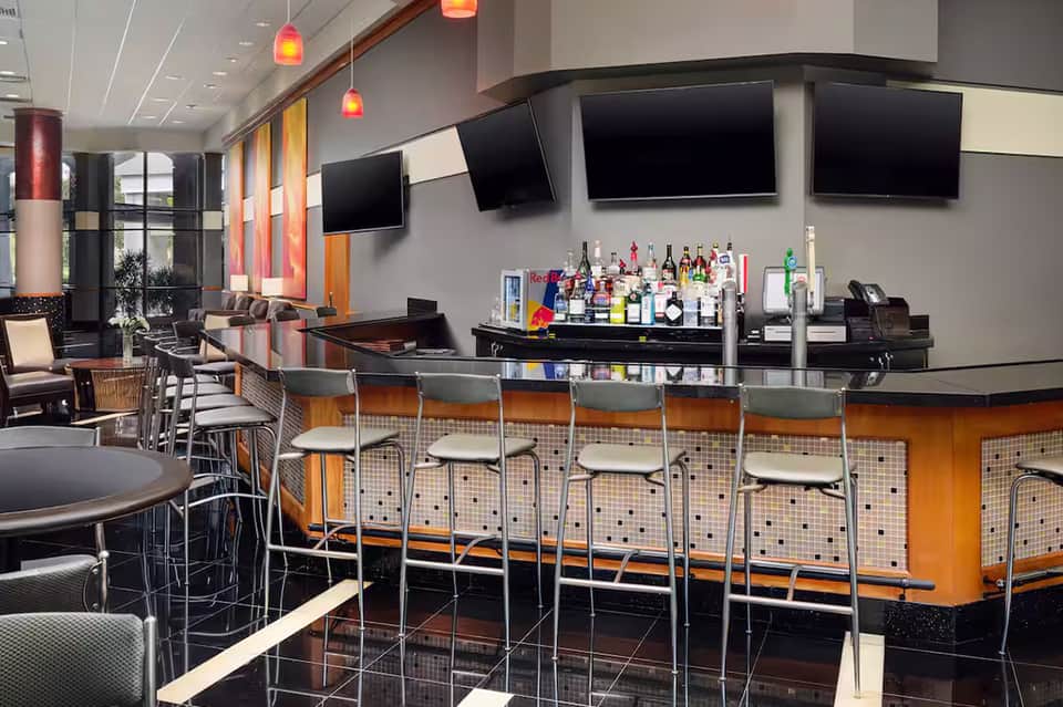 Contemporary hotel bar with orange accents, bar seating, and multiple TV screens
