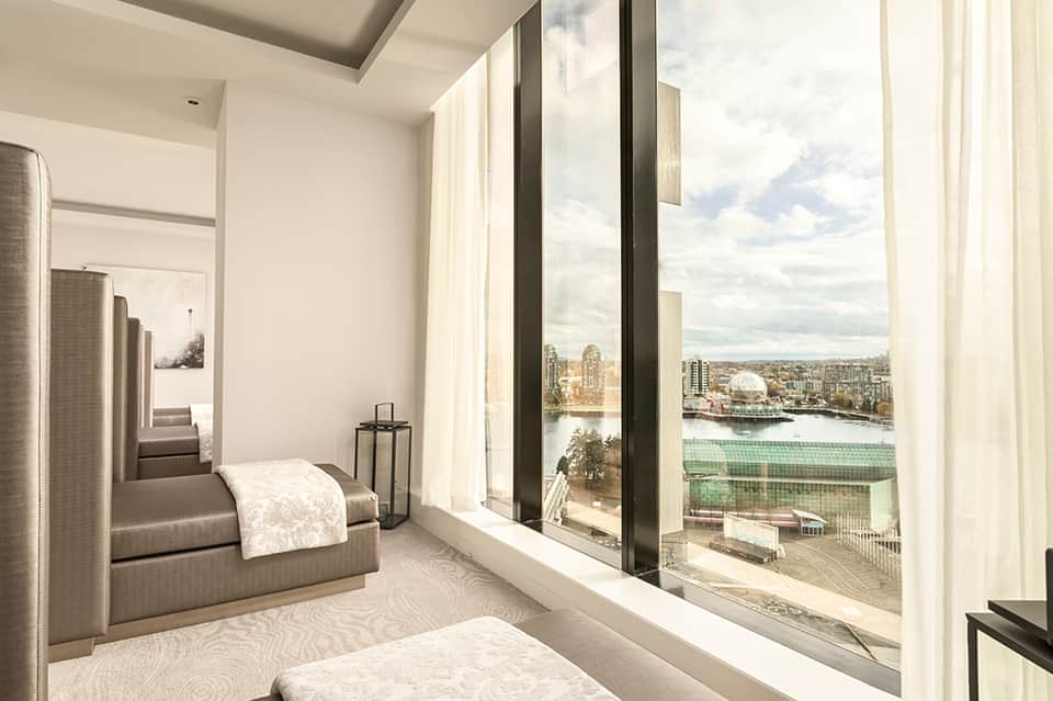 Luxury hotel bedroom with floor-to-ceiling windows overlooking cityscape with river and waterfront