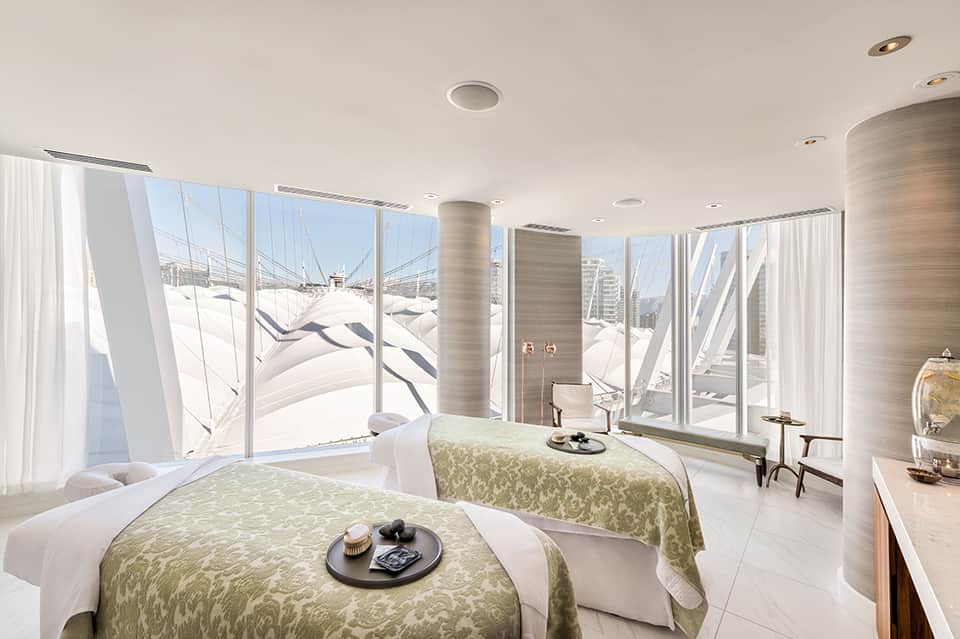 Modern hotel bedroom with twin beds, large windows overlooking marina with sailboats, minimalist design with neutral tones