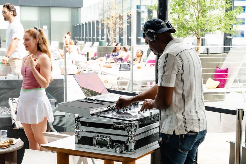 DJ performing at rooftop pool party with guests dancing and laptop visible
