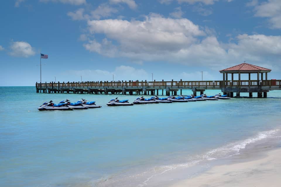 Tropical beach with turquoise water, wooden pier, jet skis, and palm trees