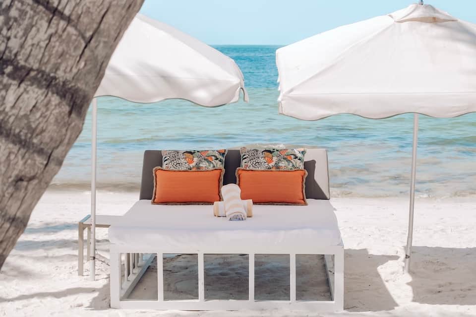 Luxury beach bed with white canopy umbrellas, decorative pillows, and ocean view