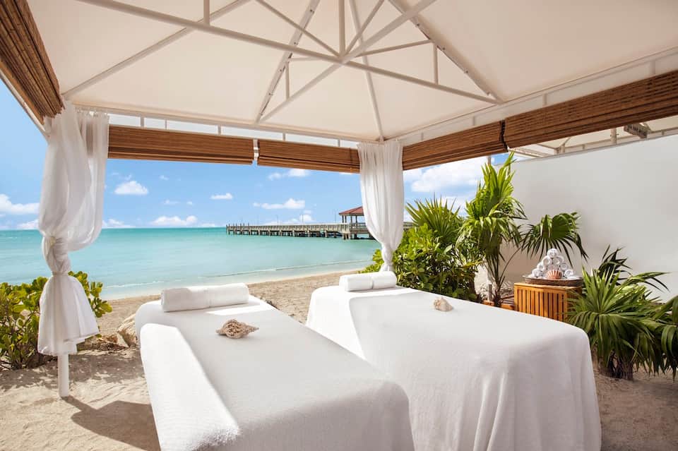 Beachfront spa pavilion with massage beds, ocean view, and tropical plants
