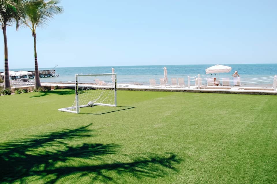 Manicured lawn with soccer goal facing pristine beach and palm trees at waterfront resort