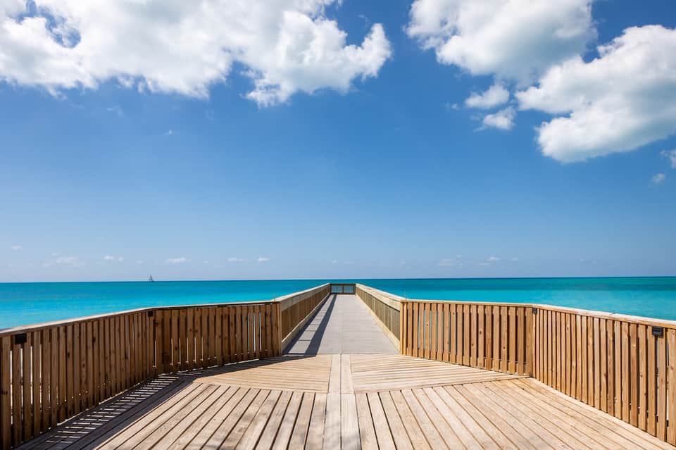 Wooden boardwalk pier extending over turquoise ocean water under blue sky