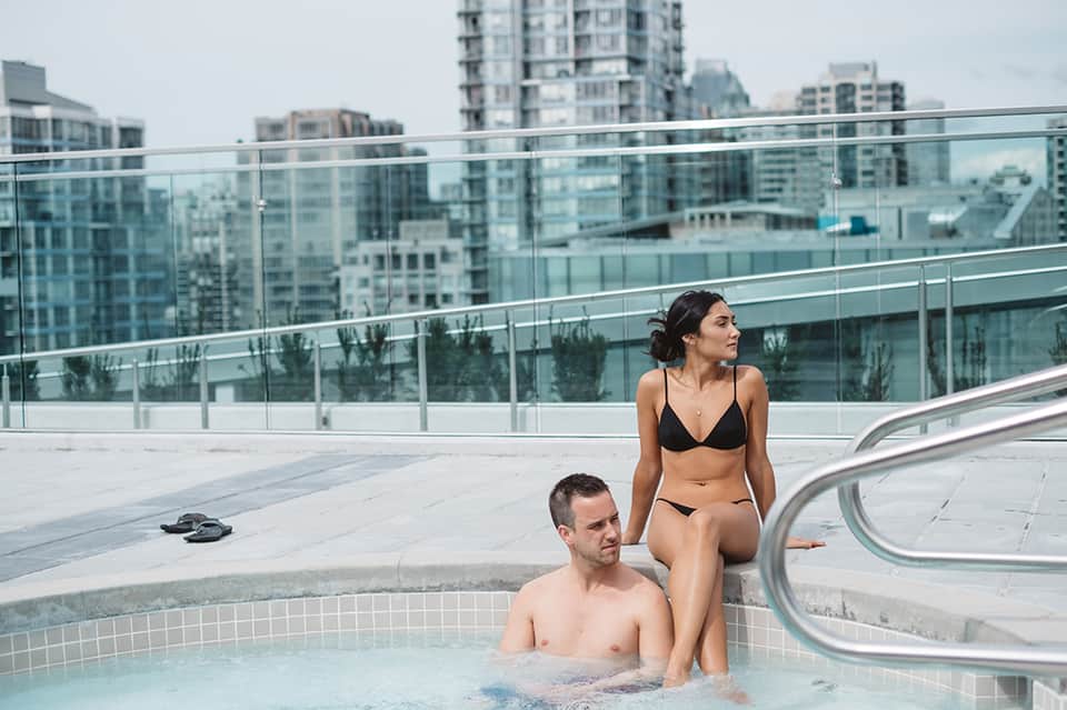 Couple relaxing in rooftop hot tub with cityscape and glass railing in background