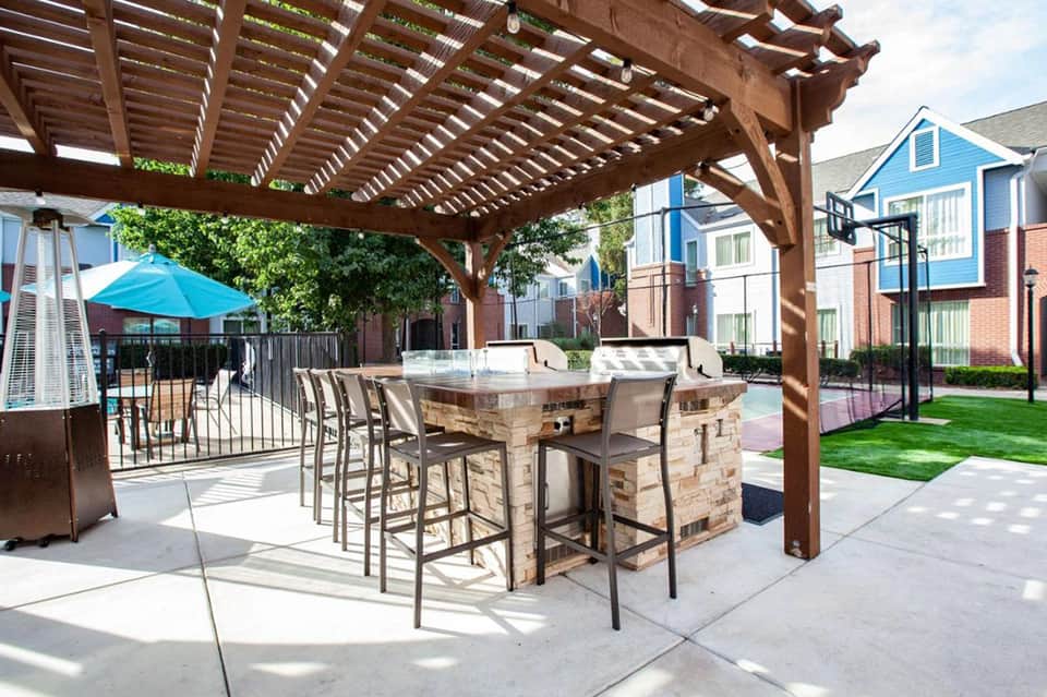 Outdoor patio with stone bar, wooden pergola, blue umbrella, and residential buildings