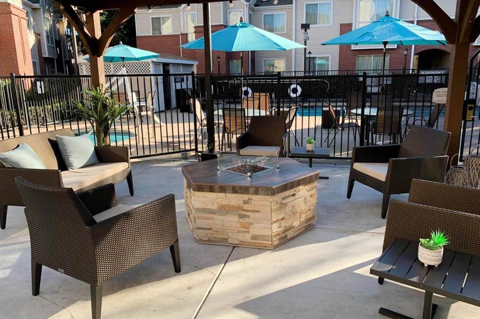 Outdoor patio with wicker chairs, fire pit, umbrellas, and pool view surrounded by residential buildings