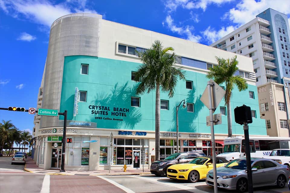 Crystal Beach Suites Hotel turquoise building exterior with cylindrical tower and palm trees on street corner