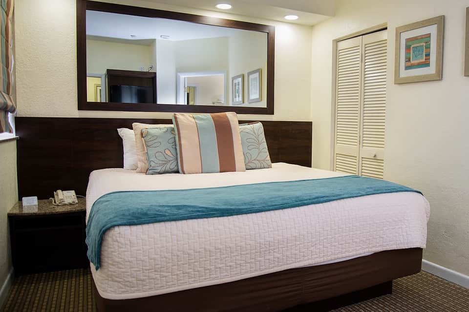 Hotel bedroom with dark wood headboard, large mirror, decorative pillows, and pale blue bedding