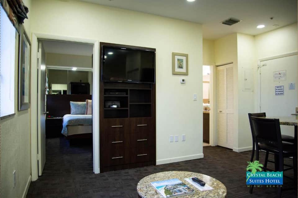 Hotel suite living area with TV, dark wood cabinet, and view into separate bedroom with bed