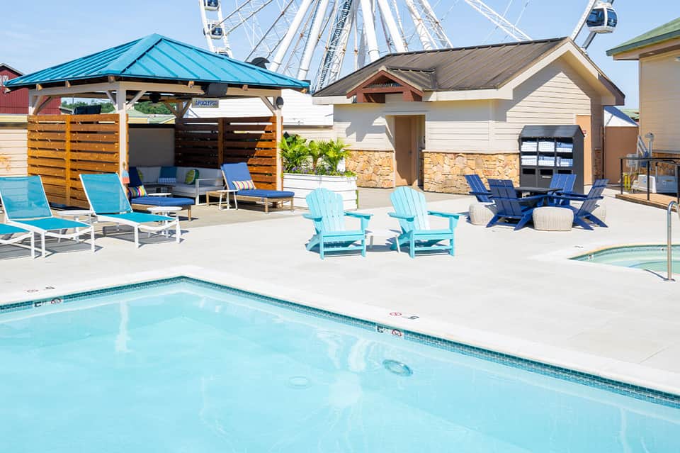 Resort pool area with turquoise water, lounge chairs, wooden cabanas, and Ferris wheel in background