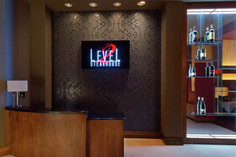 Upscale steakhouse reception area with neon sign, patterned wallpaper, wooden desk, and wine display