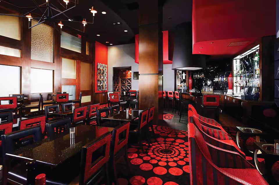 Modern restaurant interior with red and black décor, bar counter, and contemporary lighting