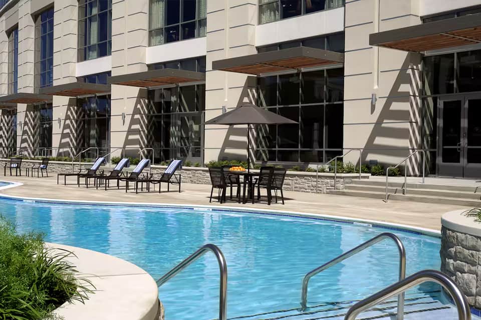 Modern hotel pool deck with loungers, dining tables, umbrellas, and contemporary building facade with geometric shadows