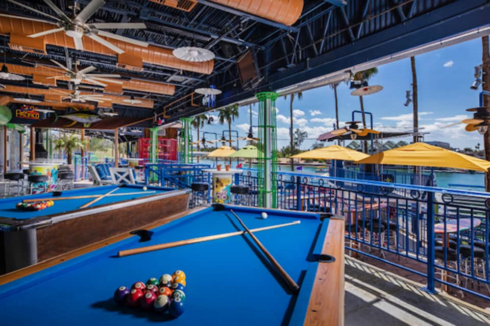 Indoor recreation area with blue pool tables, yellow umbrellas, and waterfront views through windows
